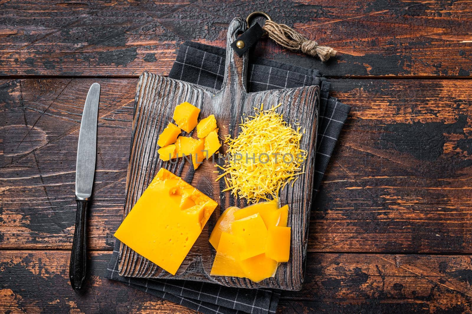 Grated and diceded Cheddar Cheese on a wooden chopping board. Dark wooden background. Top view.