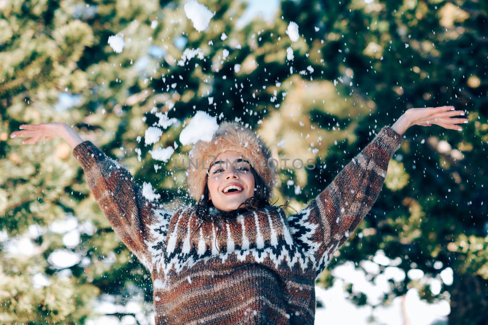 Young woman enjoying the snowy mountains in winter, in Sierra Nevada, Granada, Spain. Female wearing winter clothes playing with snow.