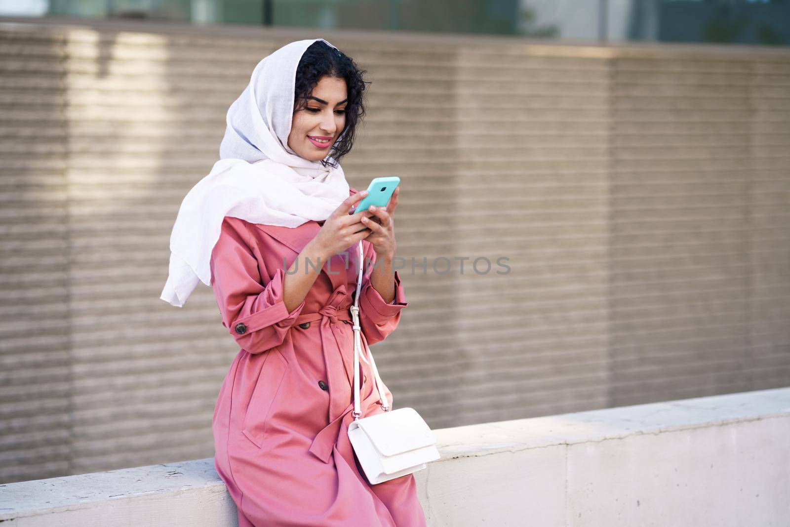Young Arab woman wearing hijab headscarf texting message with her smartphone in urban background.