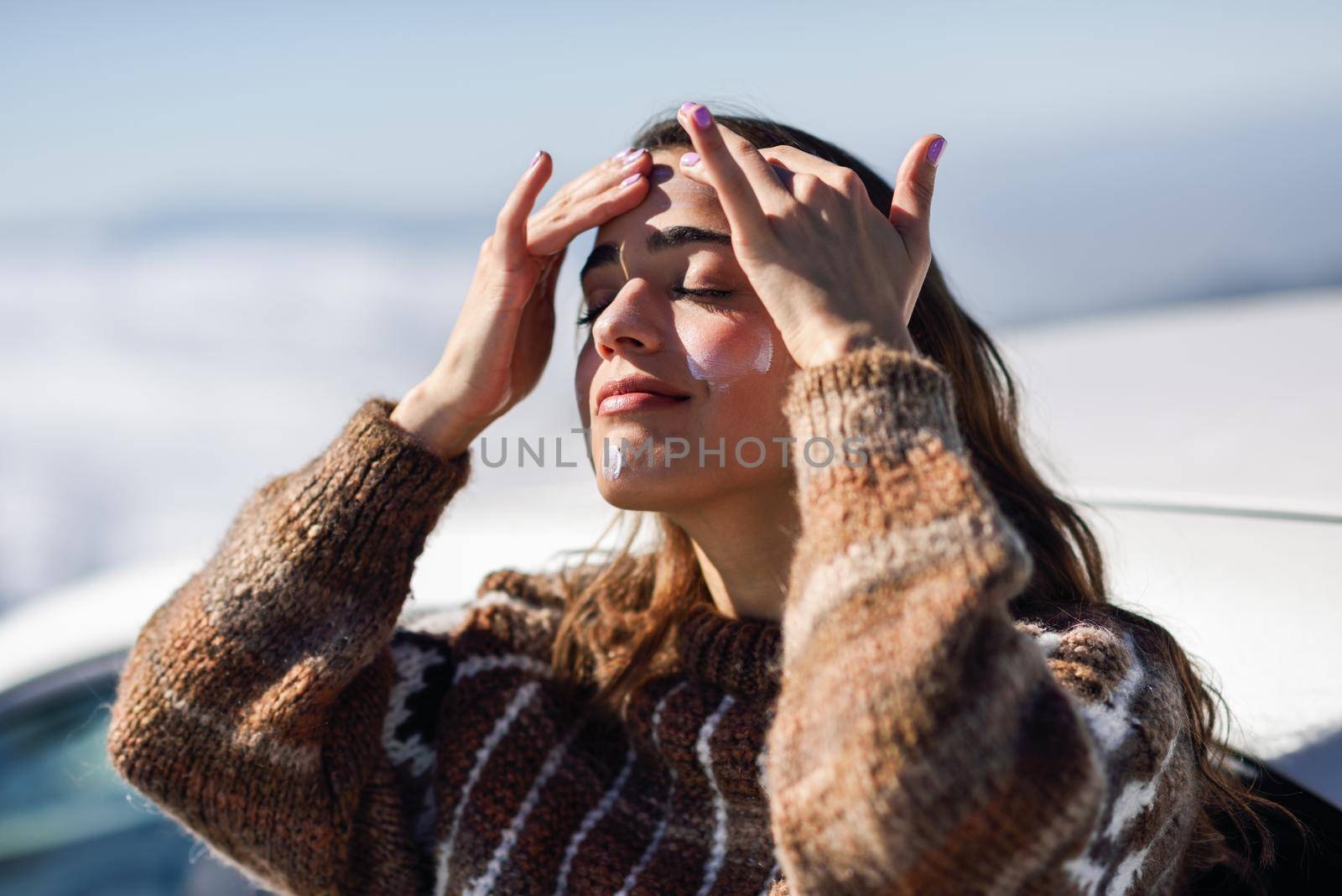 Young woman applying sunscreen on her face in snowy mountains in winter, in Sierra Nevada, Granada, Spain. Female wearing winter clothes.