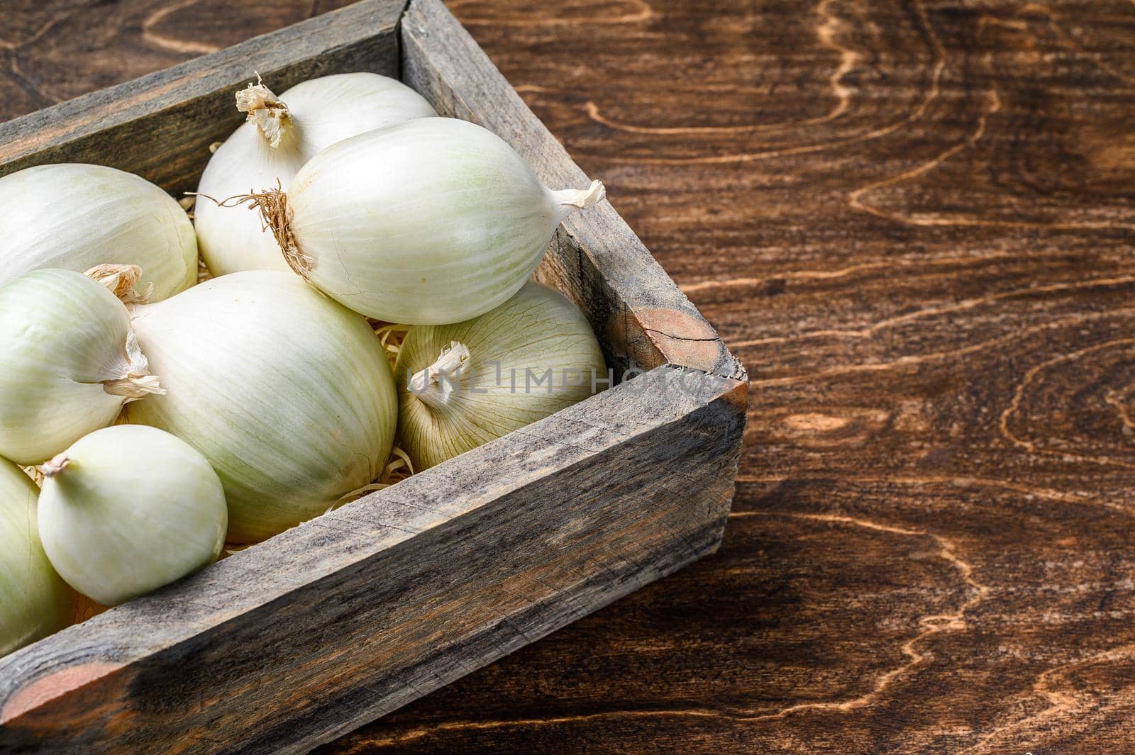 White raw onion in wooden box. Wooden background. Top view. Copy space.