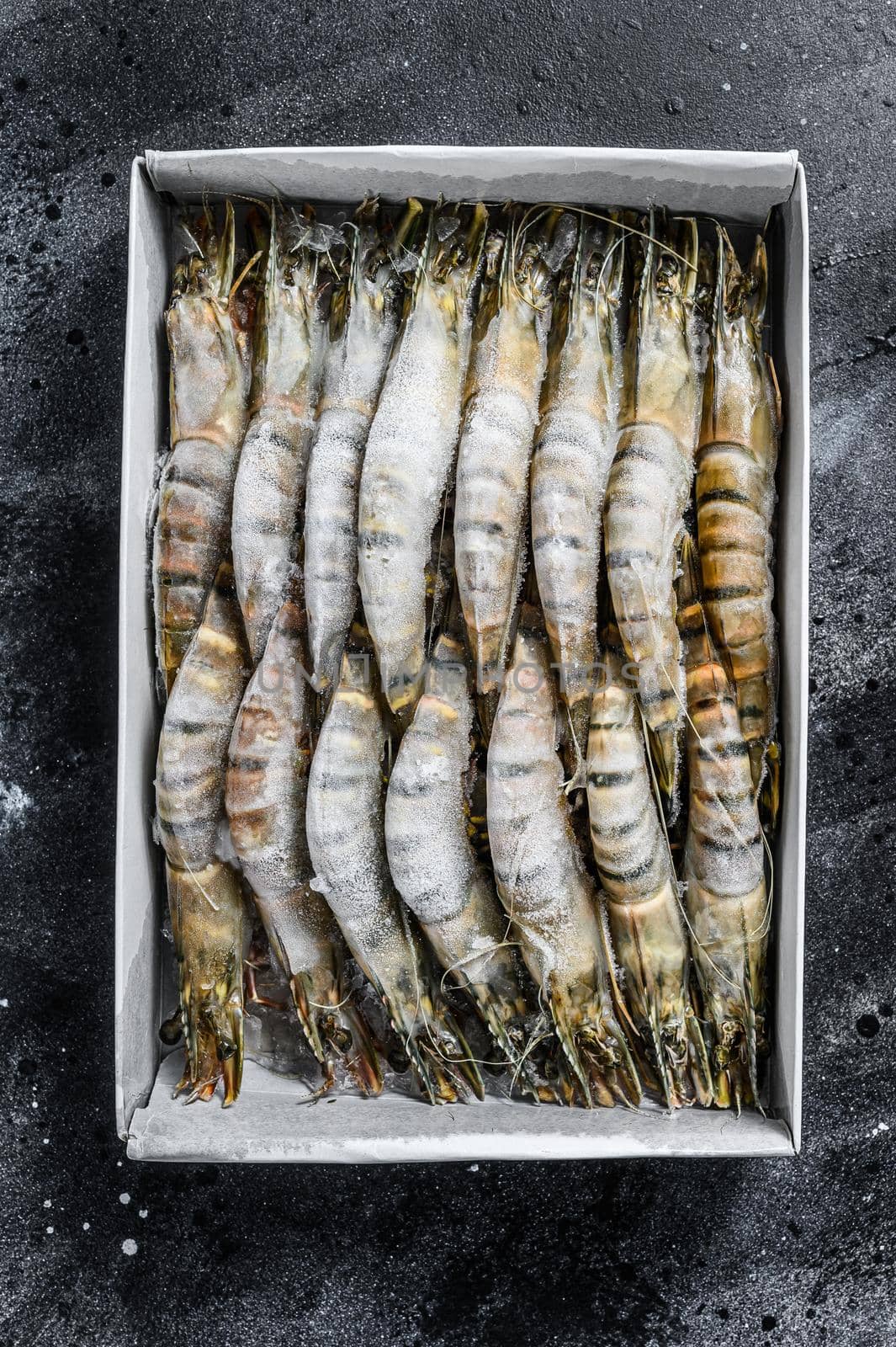 Package of frozen tiger prawns, shrimps. Black background. Top view.