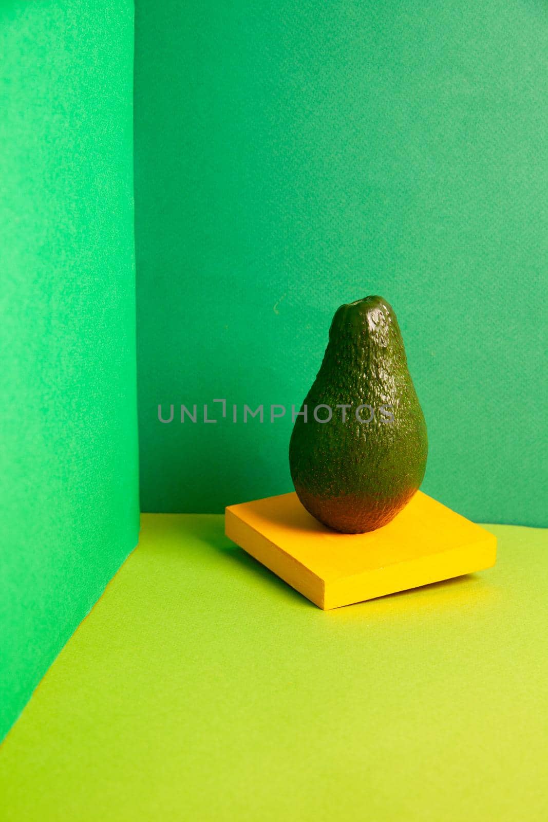 Composition of ripe green avocado arranged with yellow stand against green background