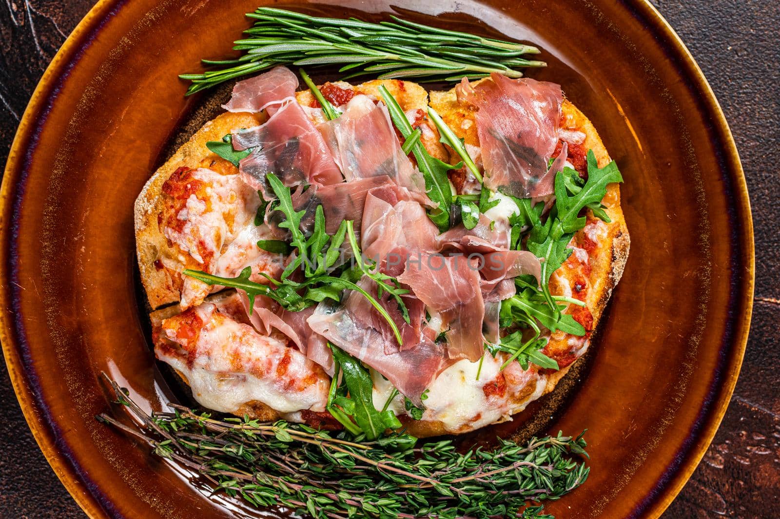 Pizza with prosciutto parma ham, arugula salad and parmesan cheese in a rustic plate. wooden background. Top view.