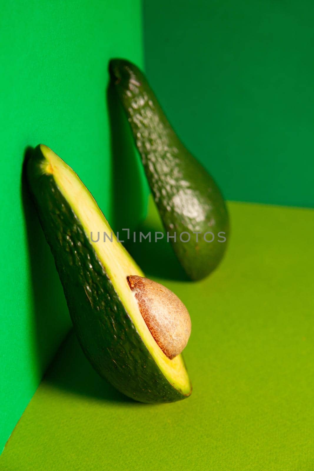 High angle of ripe fresh unpeeled halved avocado with seed leaned on green wall in studio