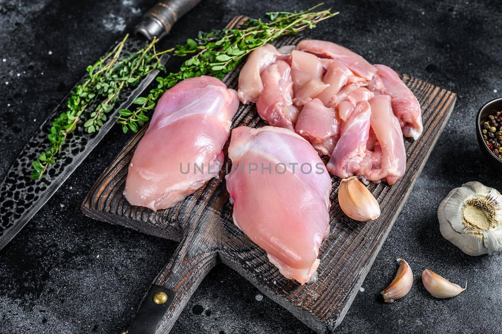 Sliced Raw Chicken thigh fillet on a wooden cutting board. Black background. Top view by Composter