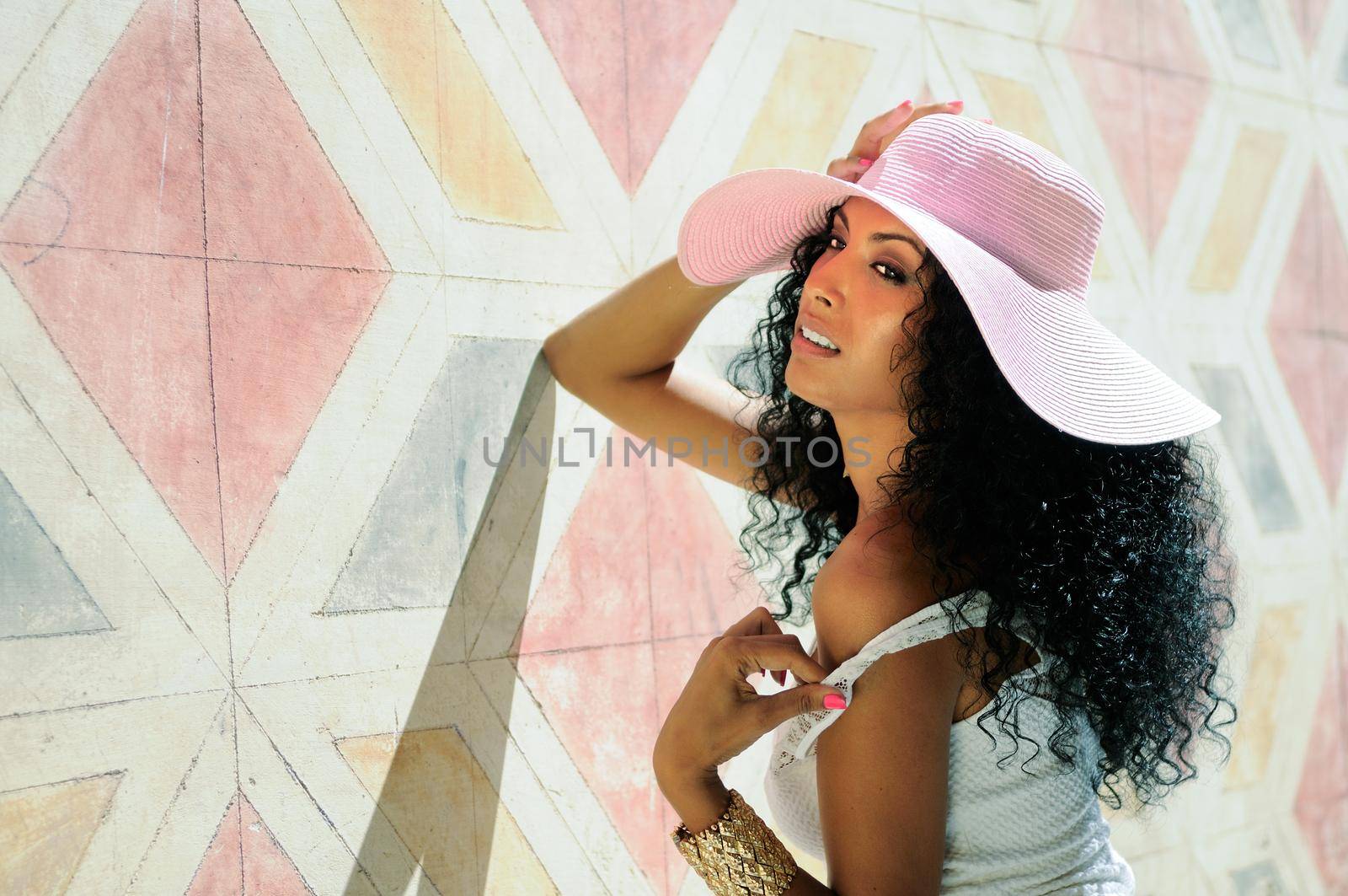 Portrait of a young black woman, model of fashion wearing dress and sun hat, with afro hairstyle in urban background