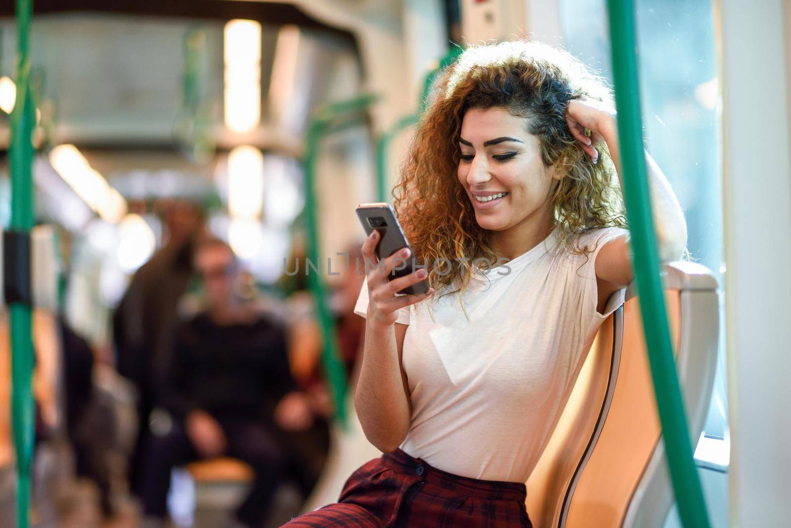 Young Arab woman inside subway train looking at her smart phone. Female in casual clothes.