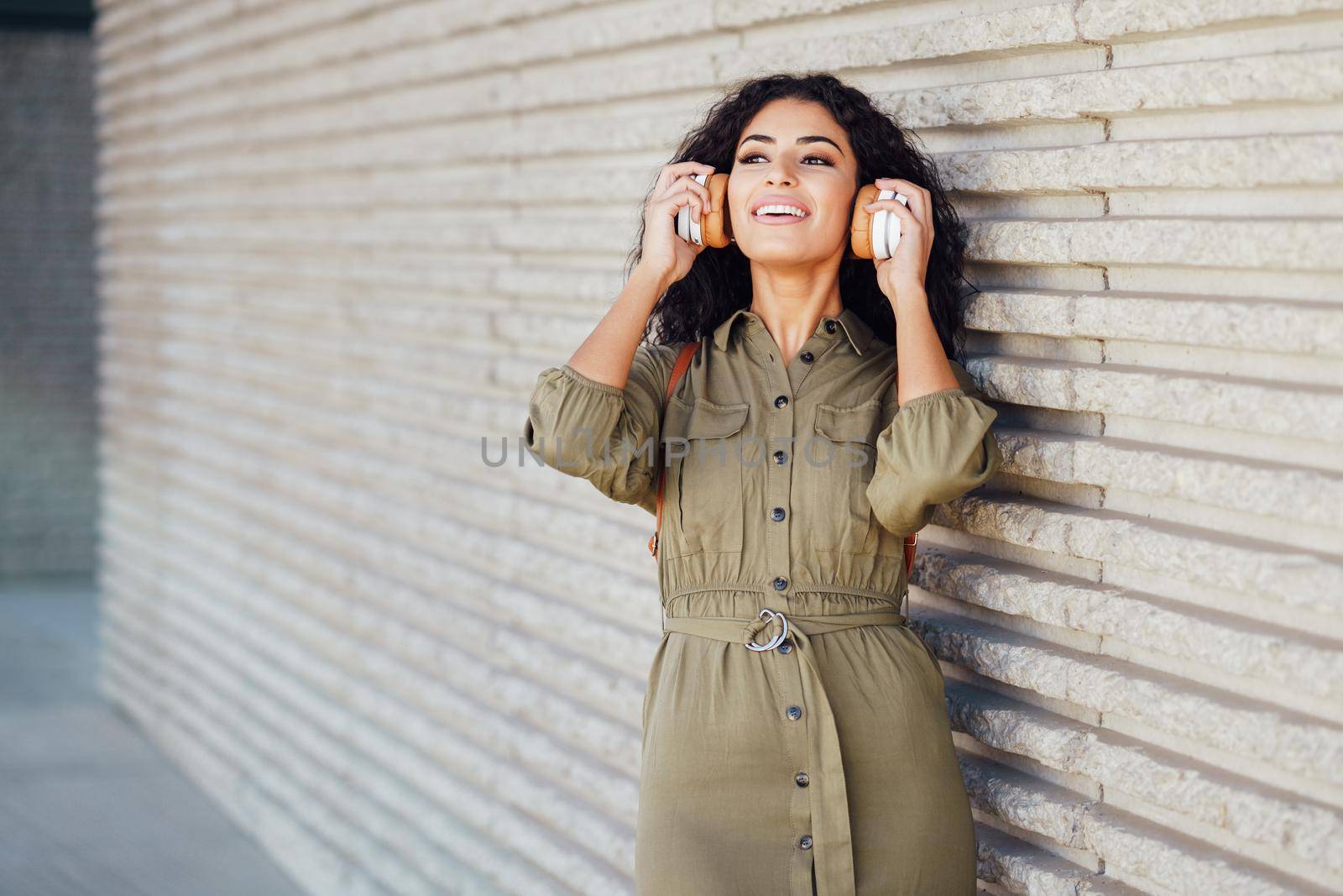 Young Arab Woman walking in the street with wireless headphones in urban background