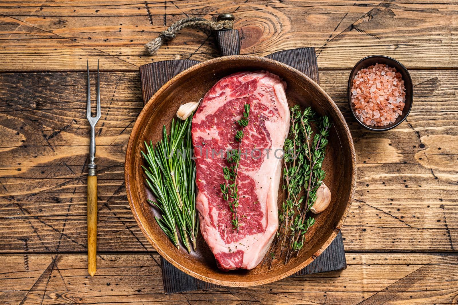 Fresh new york strip beef meat steak or striploin in a wooden plate with herbs. wooden background. Top view.