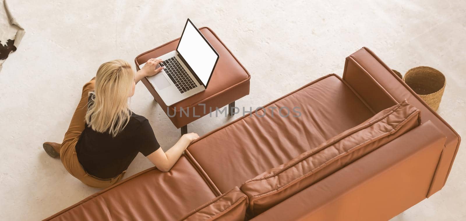 Portrait of middle age woman using her blank screen laptop while sitting back to back on the sofa at home. by Andelov13