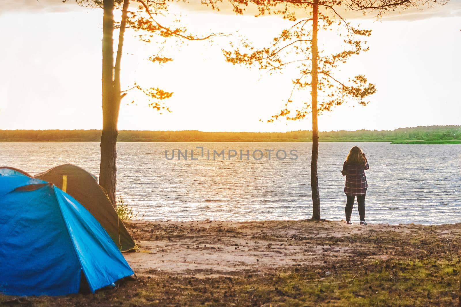 Silhouette of a girl on the background of the lake, a camp in the forest, travel and vacation in tents, camping outdoor lifestyle.