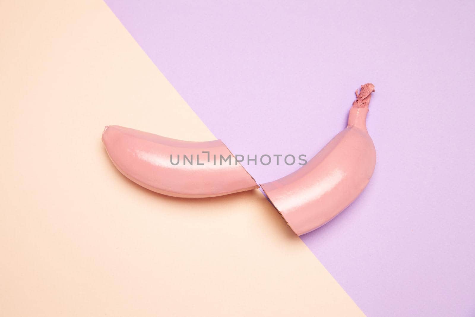 From above of halved unpeeled banana painted in pink color arranged on two color background