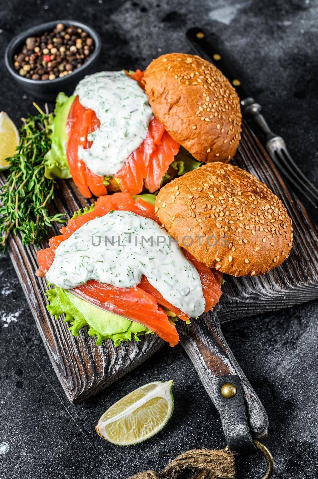 Fish burger with salted salmon, avocado, mustard sauce, cucumber and Iceberg salad. Black background. top view by Composter