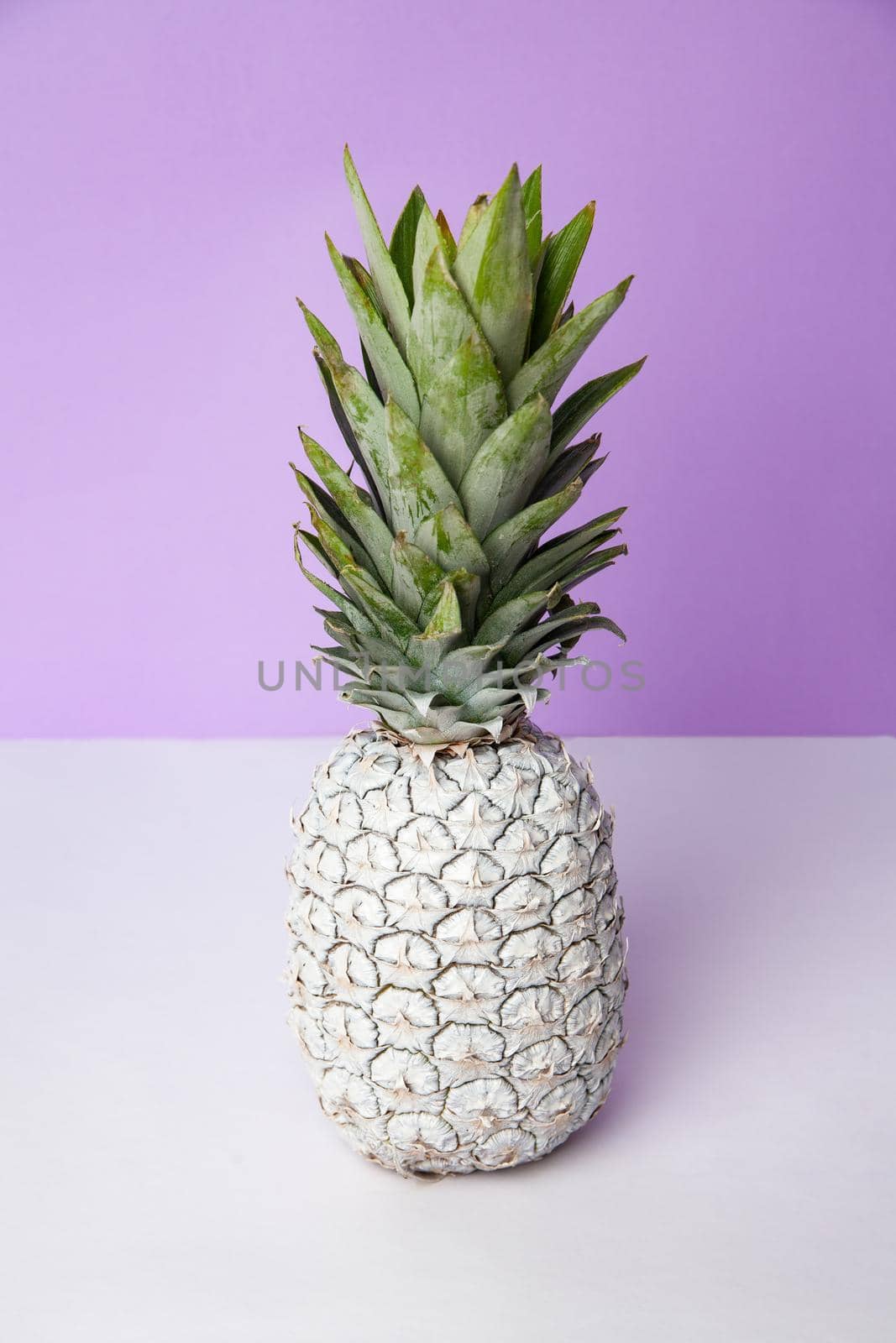 White pineapple on table in studio on violet background by Julenochek