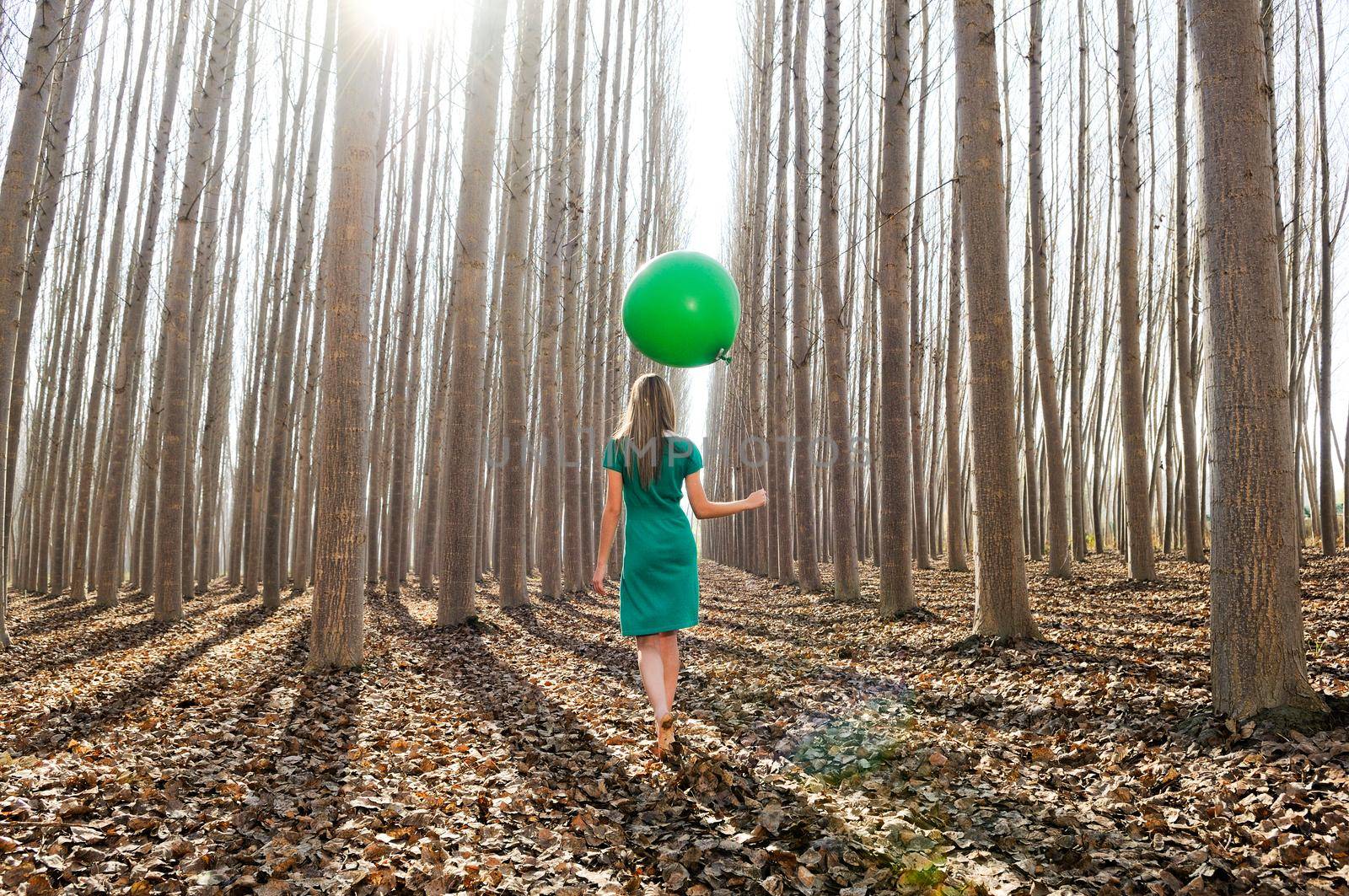 Beautiful blonde girl, dressed in green, walking into the forest