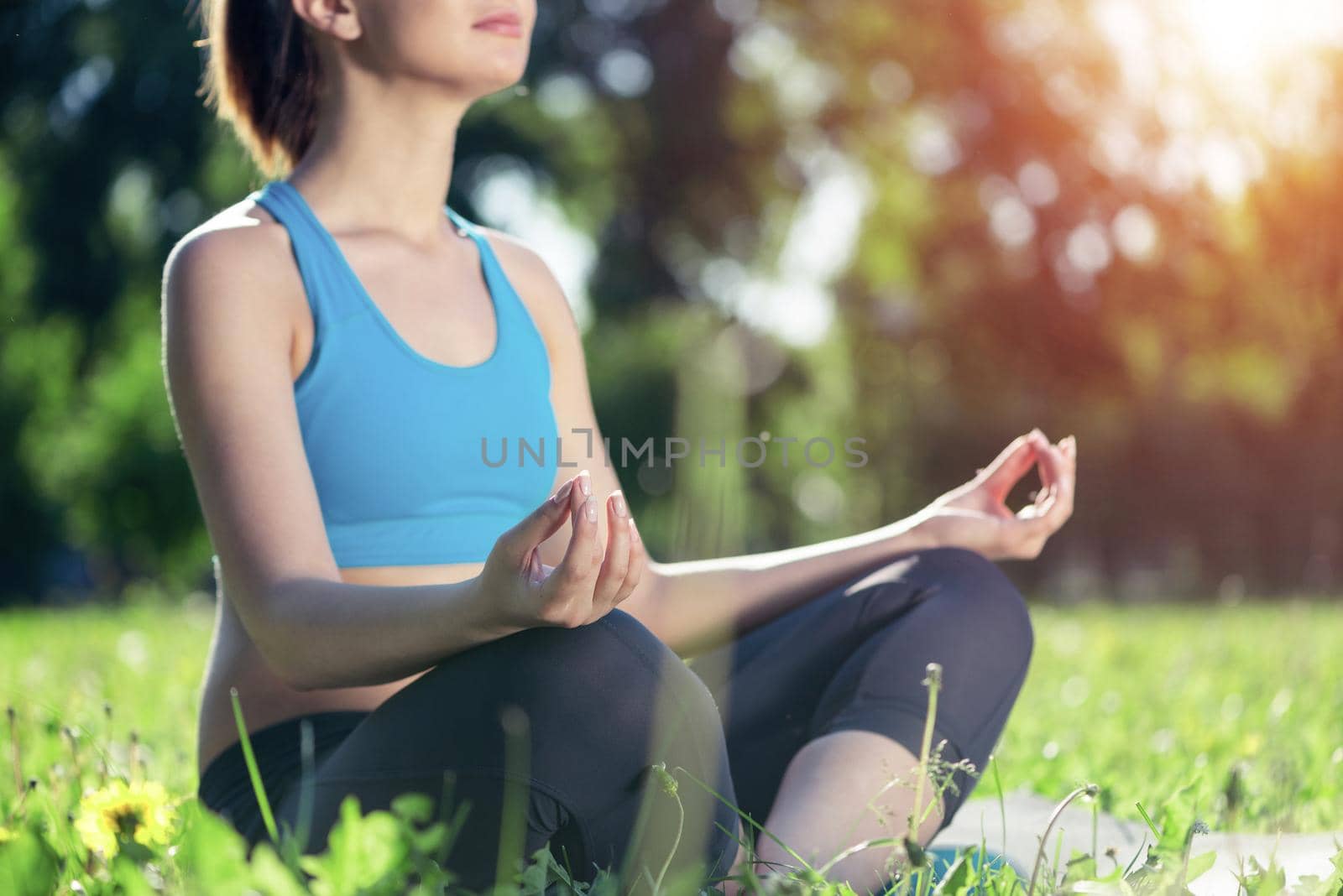 Girl meditates in lotus pose on green grass. Practicing of yoga concept. Young woman body in sportswear without head. Training and meditation outdoor at summer day. Healthy lifestyle and relaxation.