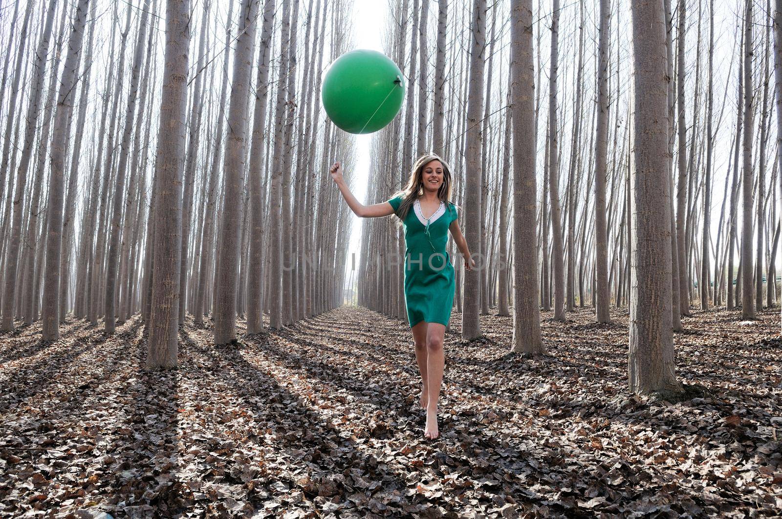 Beautiful blonde girl, dressed in green, walking into the forest