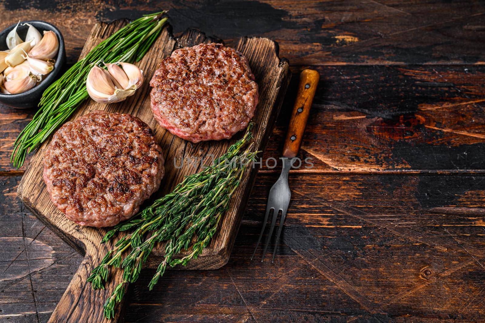 Barbecue steak patties for burger from ground beef meat on a wooden cutting board. Dark wooden background. Top view. Copy space by Composter