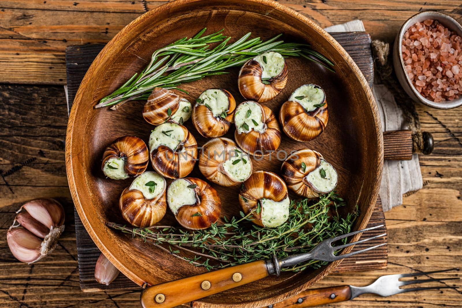 French Escargot Snails with garlic butter in a wooden plate. Wooden background. Top view by Composter