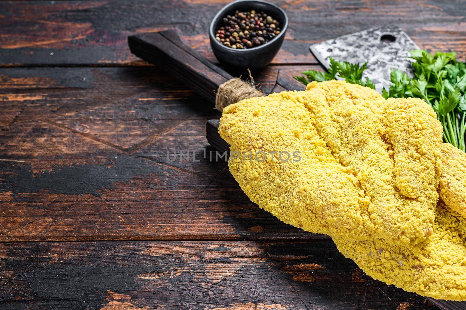Raw large Viennese schnitzel on a cutting board. Black wooden background. Top view. Copy space by Composter