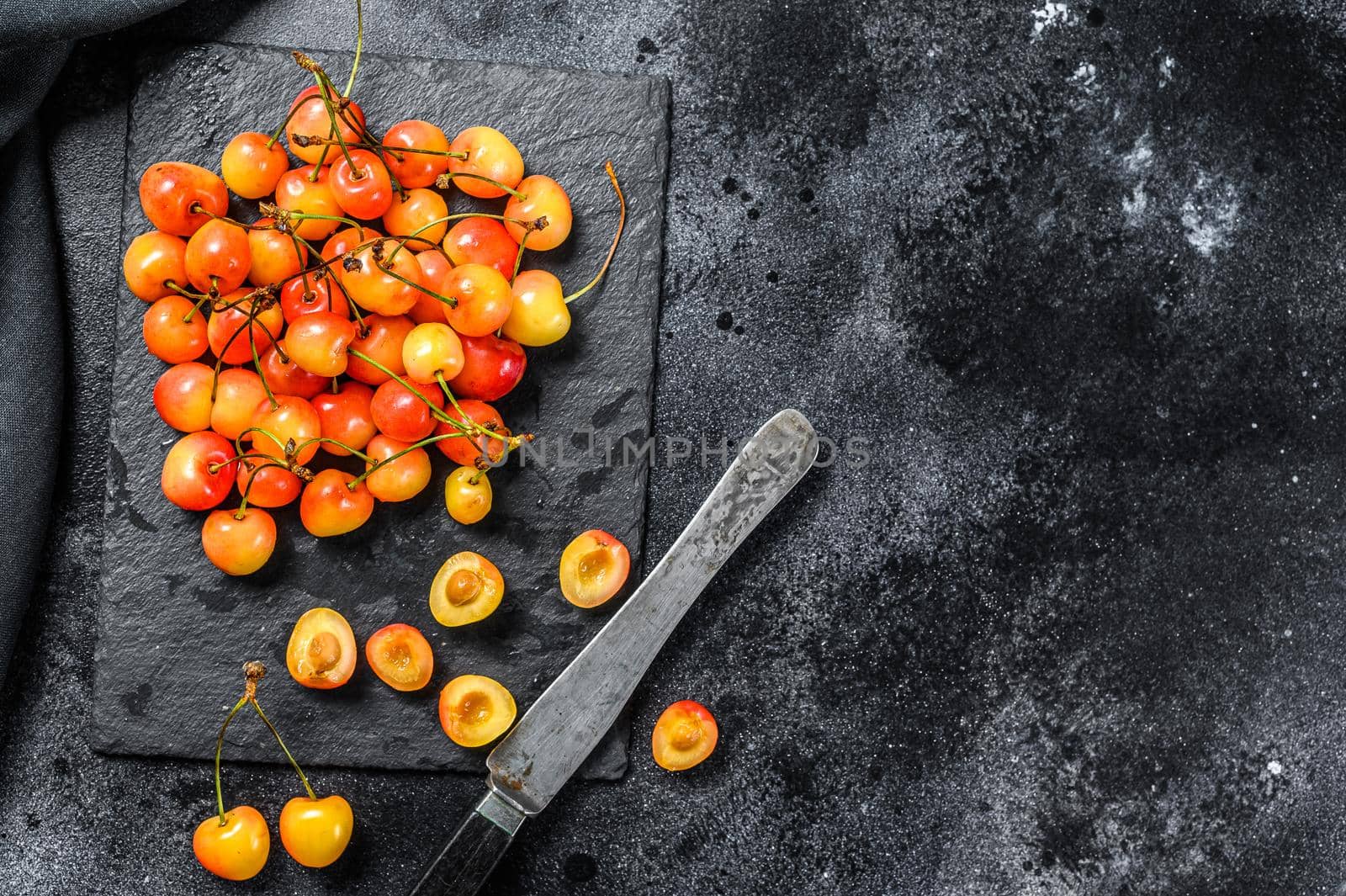 Mix of yellow and red ripe cherries. Black background. Top view. Copy space.