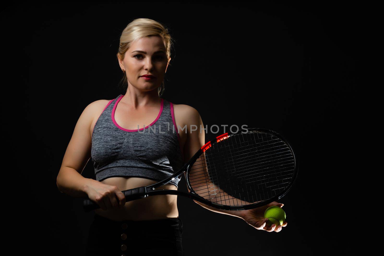 Young female tennis player posing with racket on black background