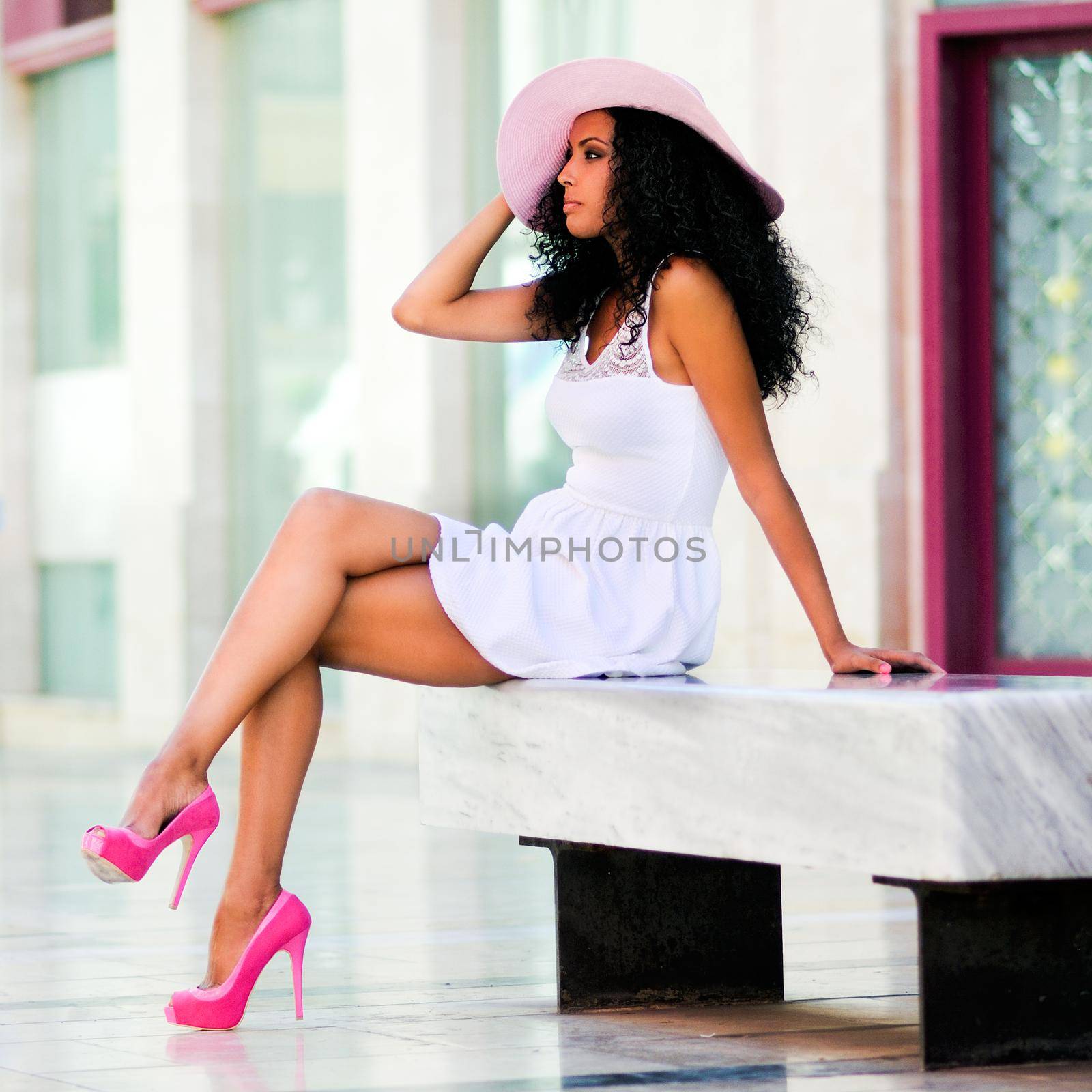 Portrait of a young black woman, model of fashion wearing dress and sun hat, with afro hairstyle in urban background