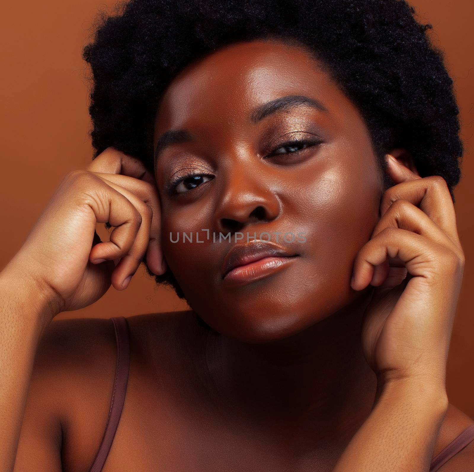 pretty young african american woman with curly hair posing cheerful gesturing on brown background, lifestyle people concept close up