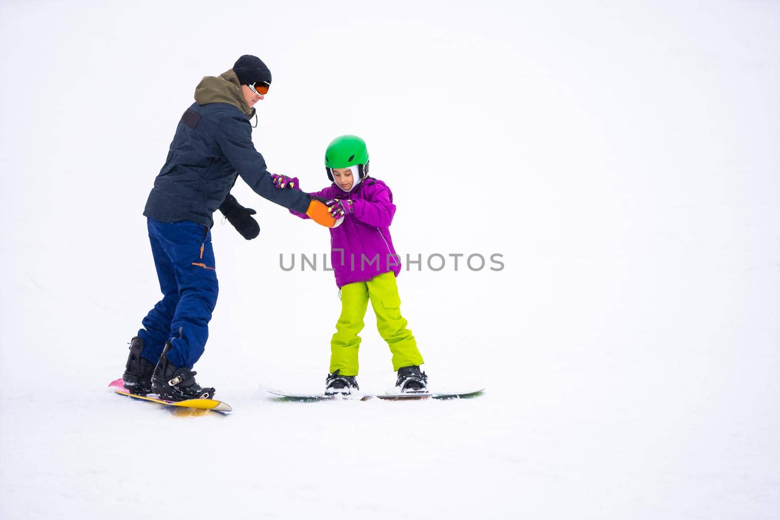 Instructors teach a child on a snow slope to snowboard by Andelov13