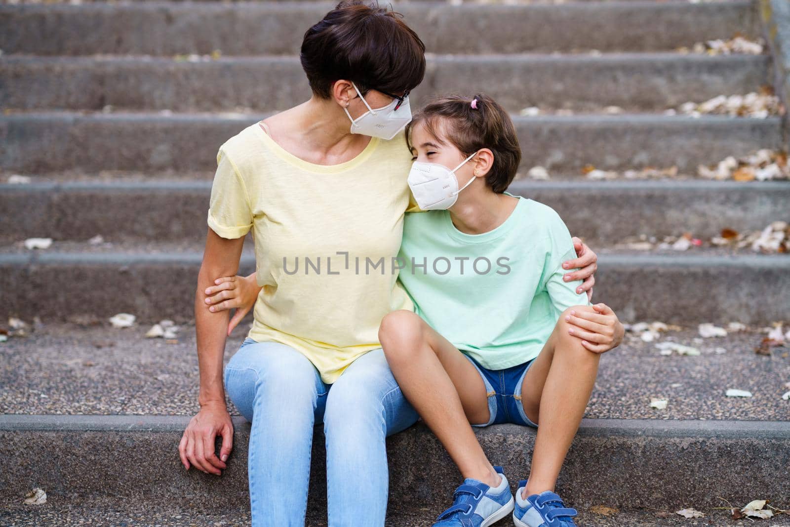 Middle-aged mother and daughter sit on the street wearing masks by javiindy