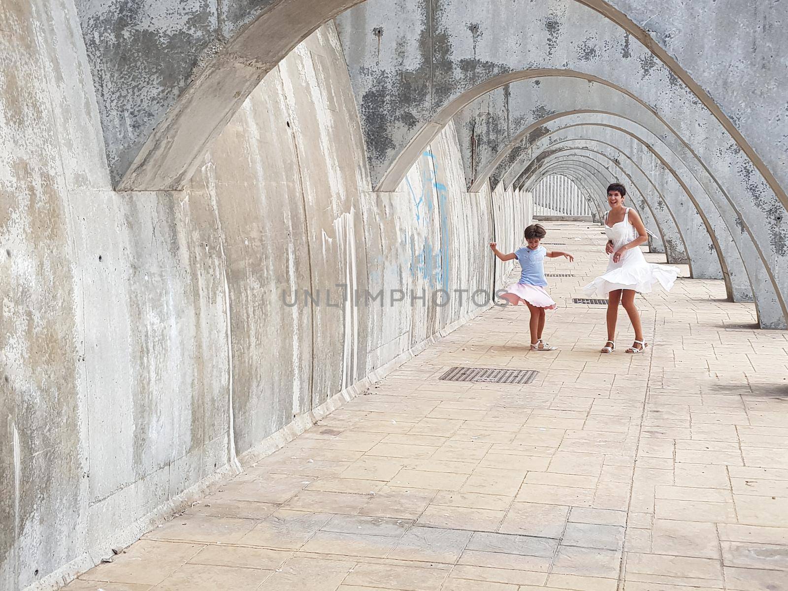 Funny mother and daughter dancing under the arches of the Port of Malaga in Andalusia, Spain. Females wearing dress.