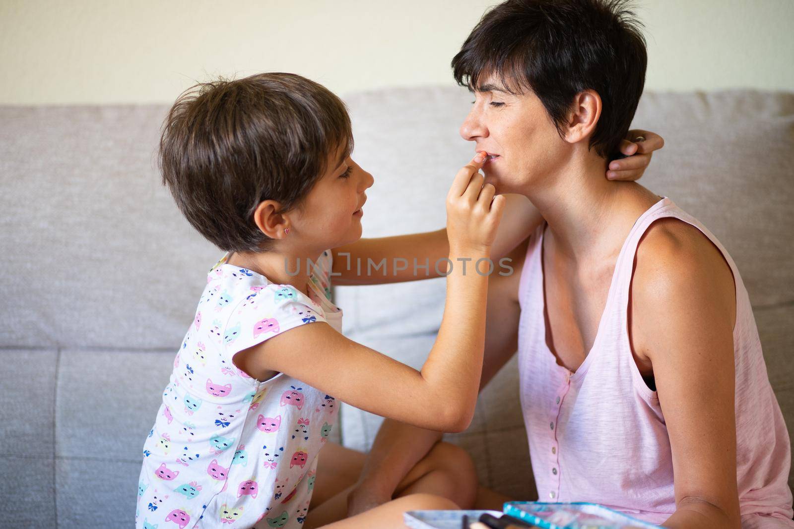 Happy beautiful mother and her little cute daughter doing make up for each other. Mum spending free time with her daughter.