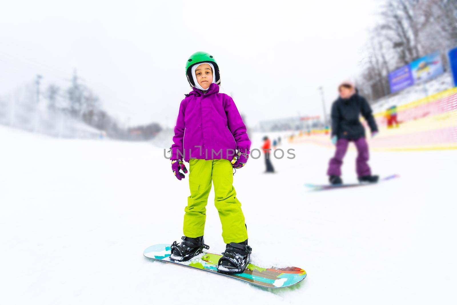Snowboard Winter Sport. little girl learning to snowboard, wearing warm winter clothes. Winter background.