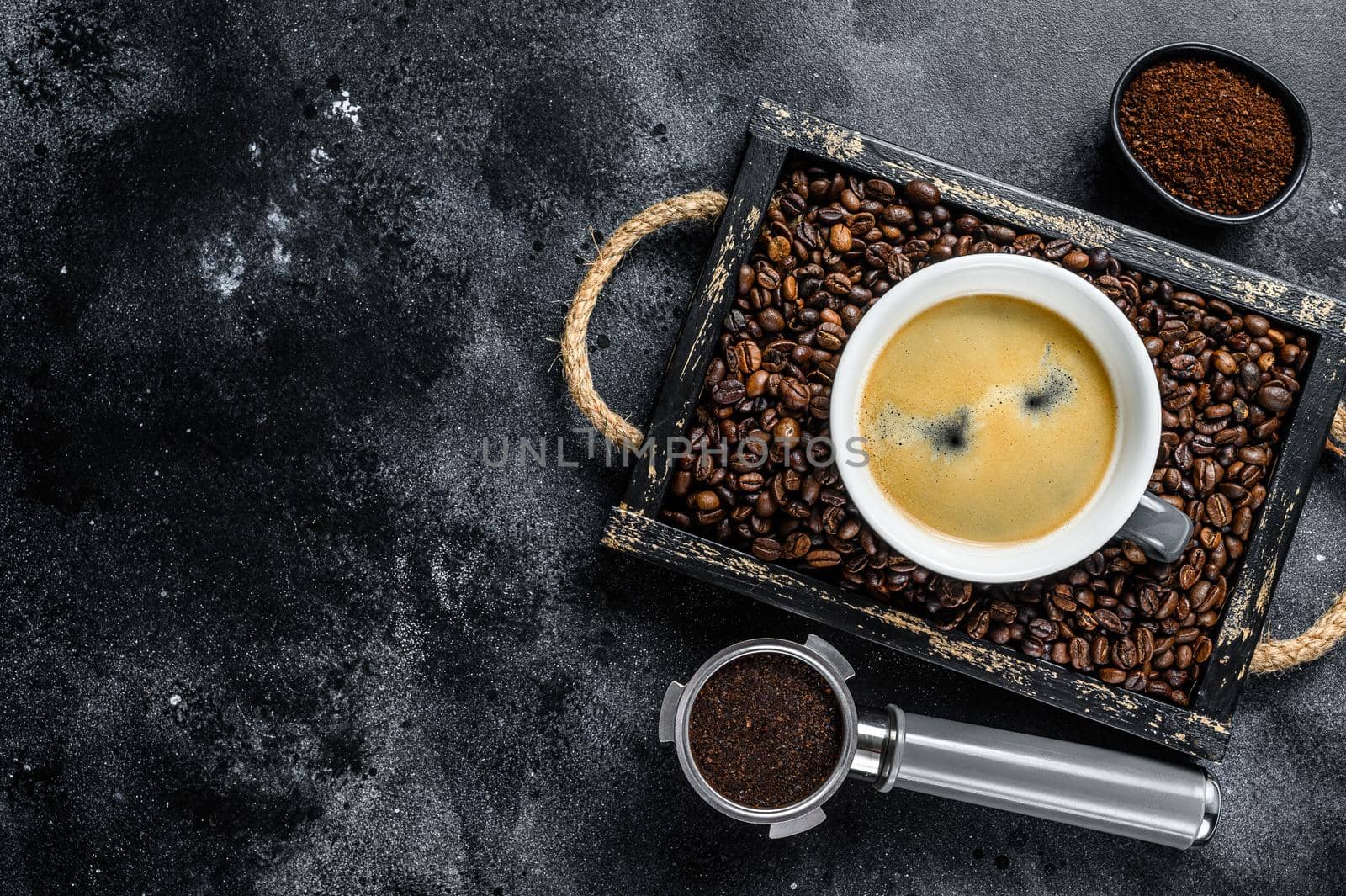 Coffee cup and beans in old wooden tray. Black background. Top view. Copy space by Composter
