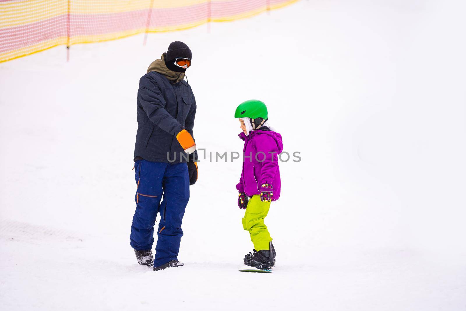 At Cold Winder Day at Mountain Ski Resort Father Teaching Little Daughter Snowboarding