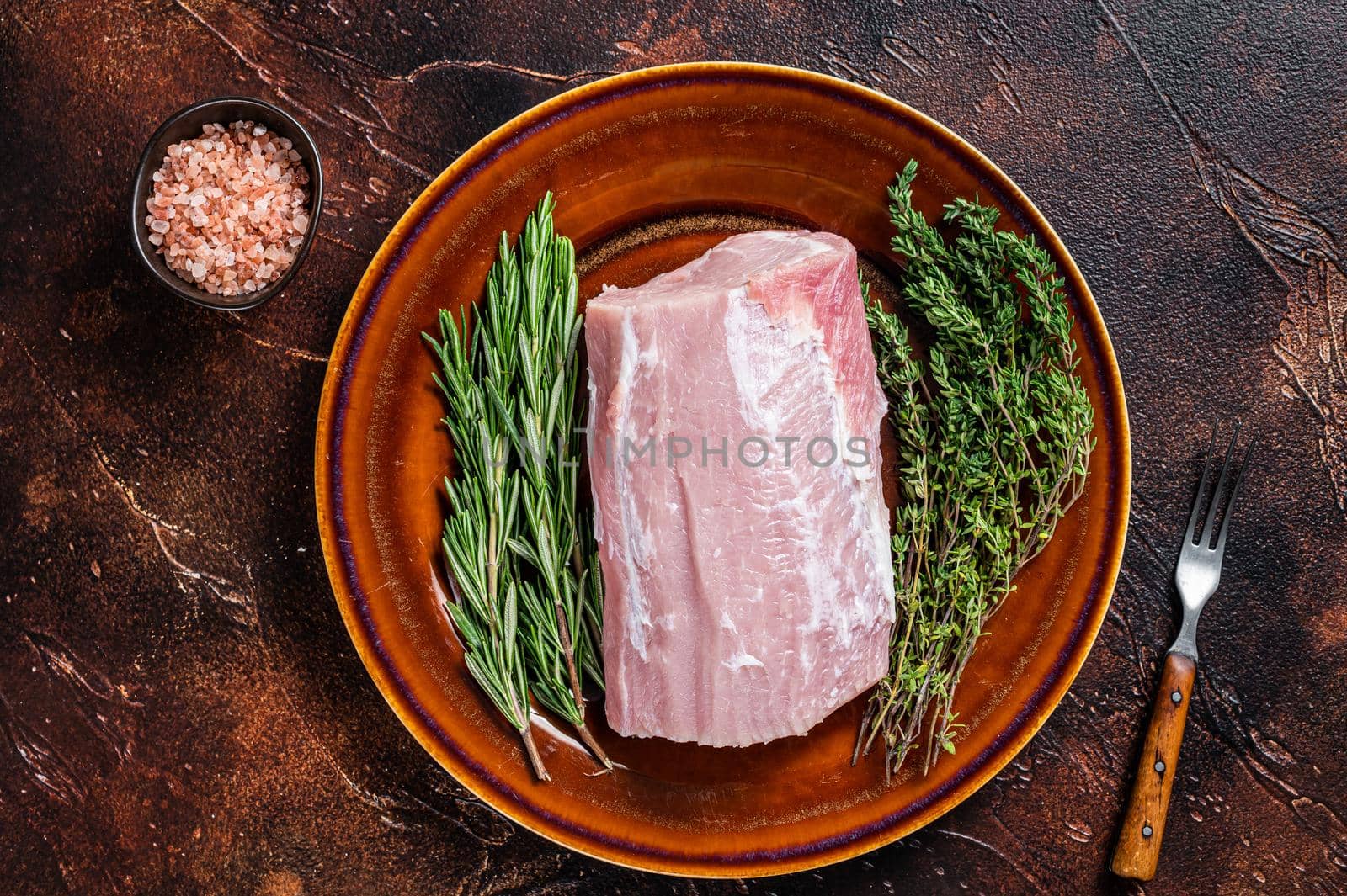 Fresh Raw pork loin meat with thyme and rosemary on rustic plate. Dark background. Top view by Composter