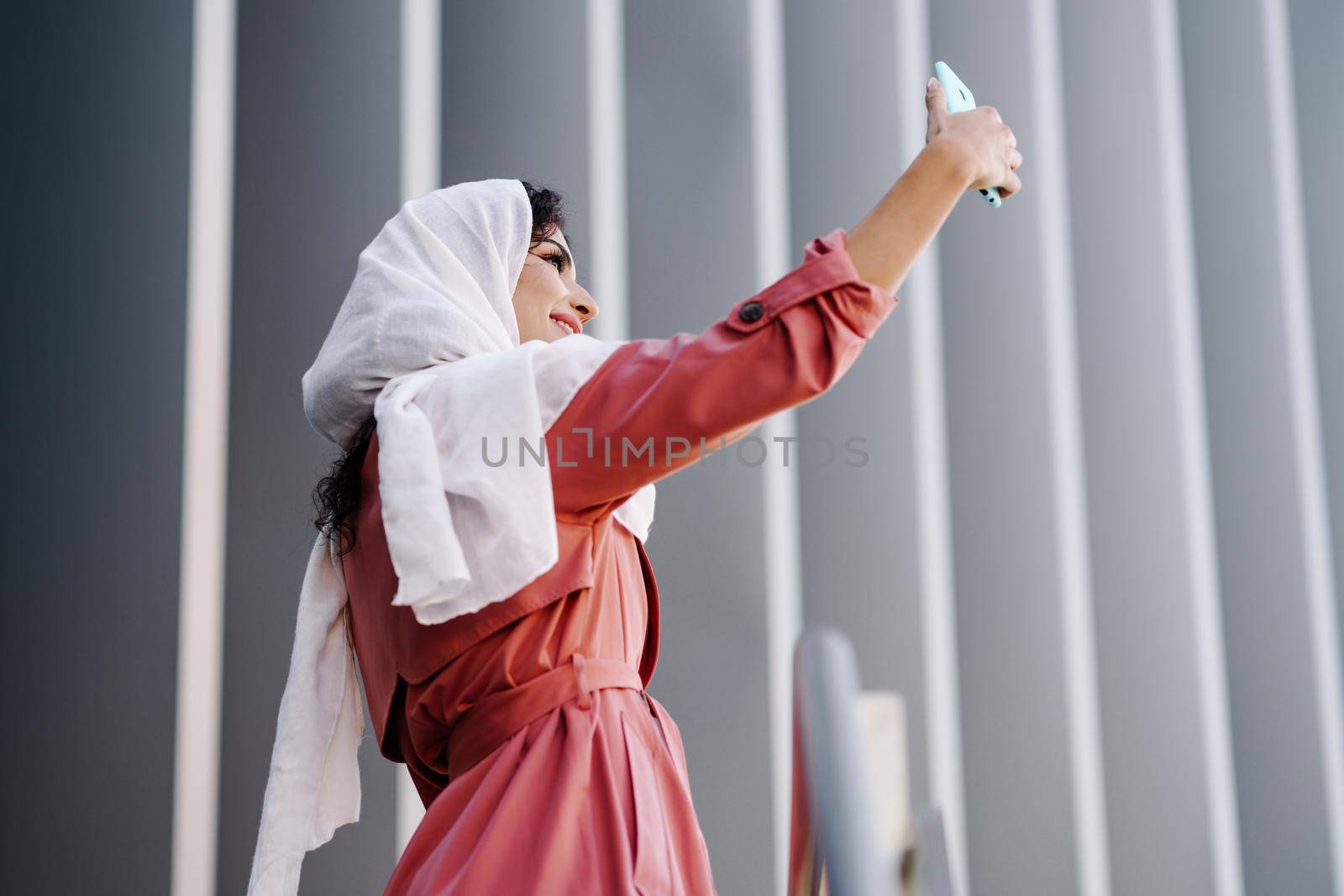 Young Arab Woman wearing hijab headscarf photograph with a smartphone outdoors.