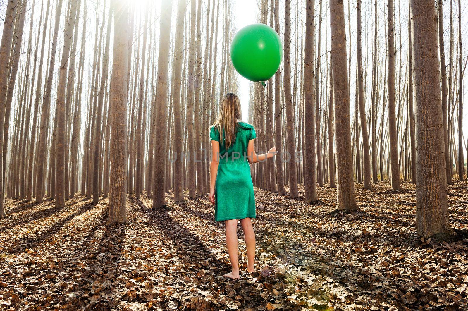 Beautiful blonde girl, dressed in green, standing in the forest