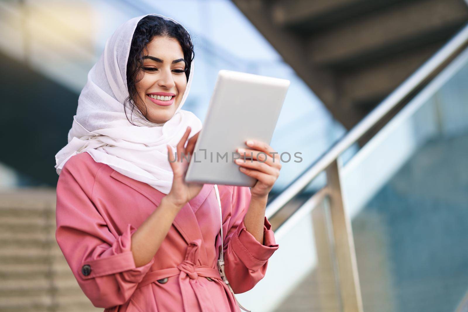 Young Arab woman wearing hijab using digital tablet outdoors by javiindy