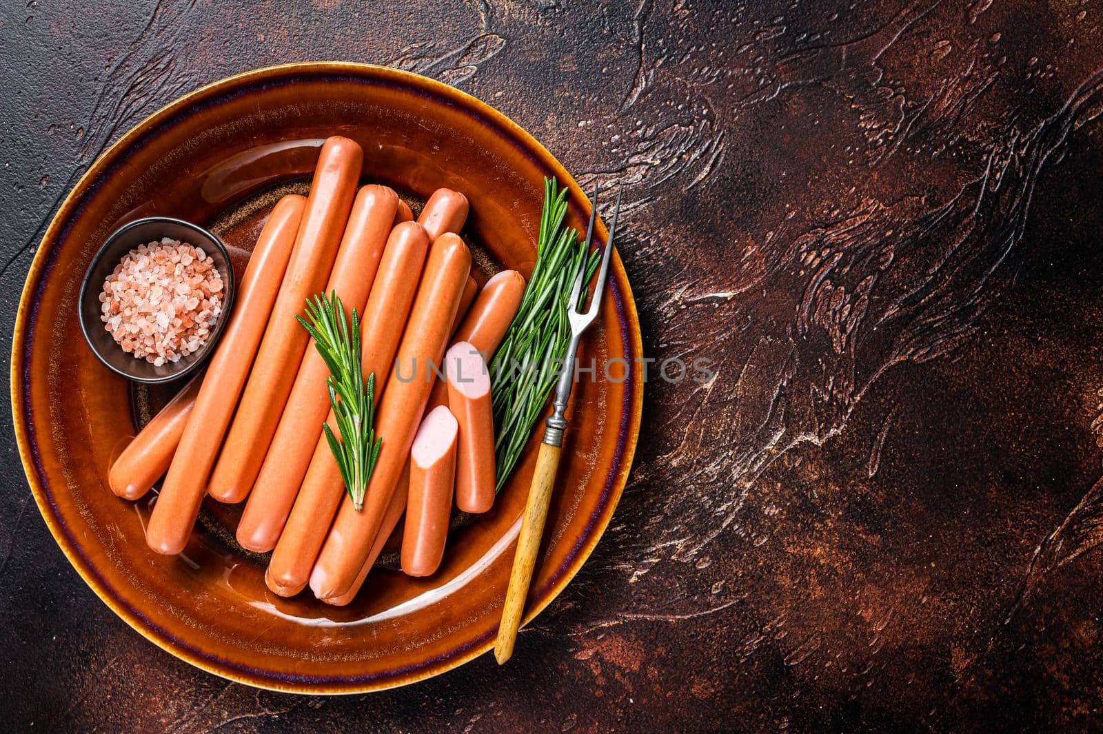Frankfurter raw sausages in a rustic plate with herbs. Dark background. Top view. Copy space by Composter