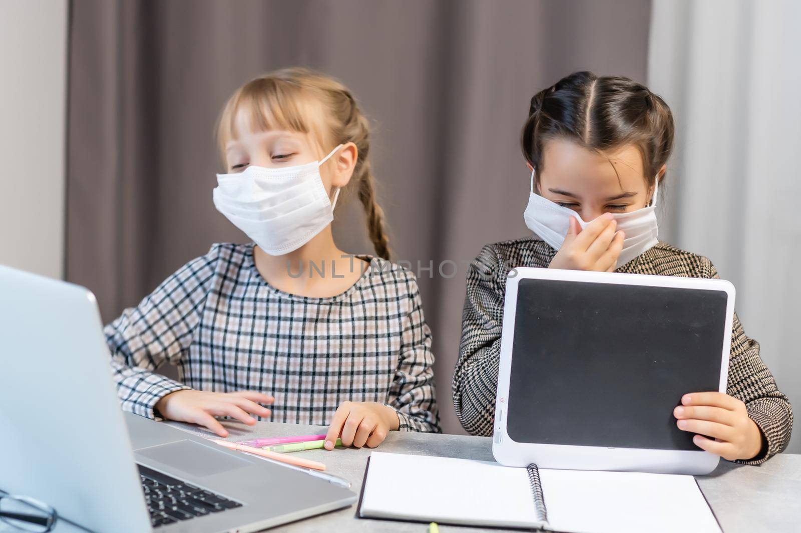 Young elementary school girls with face protective mask watching online education class. Coronavirus or Covid-19 lockdown education concept.