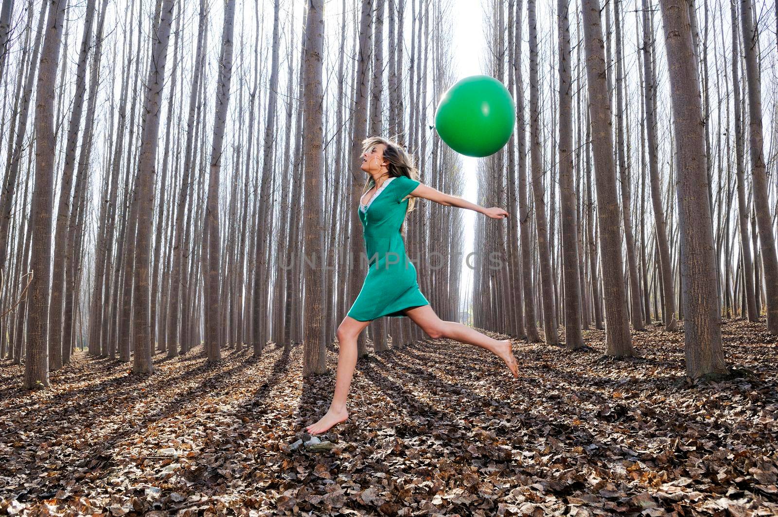 Beautiful blonde girl, dressed in green, jumping into the woods with a balloon. by javiindy
