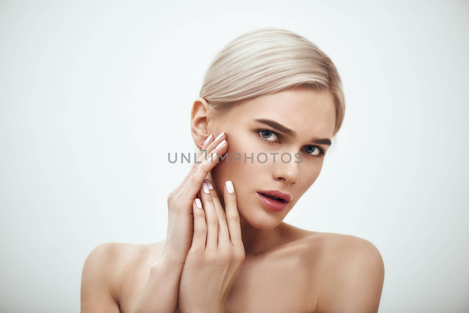 Natural beauty. Portrait of gorgeous blonde woman touching her perfect soft skin while standing against grey background. Skin care. Cosmetics concept