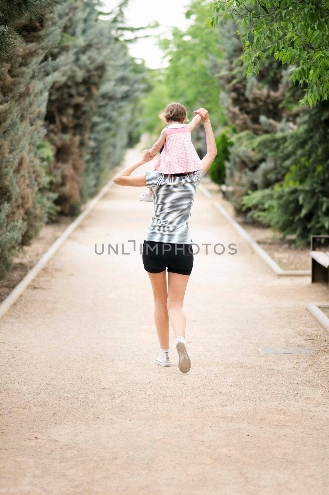 Little girl walking on the shoulders of her mother in the park