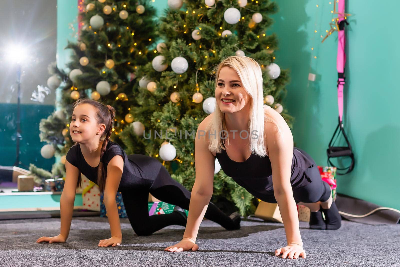 mother and daughter doing fitness near the christmas tree at gym. New Year. Christmas, holidays, fitness, and gym concept.