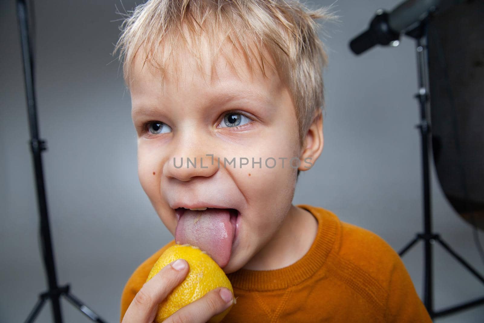 Adorable kid licking halved lemon in studio by Julenochek