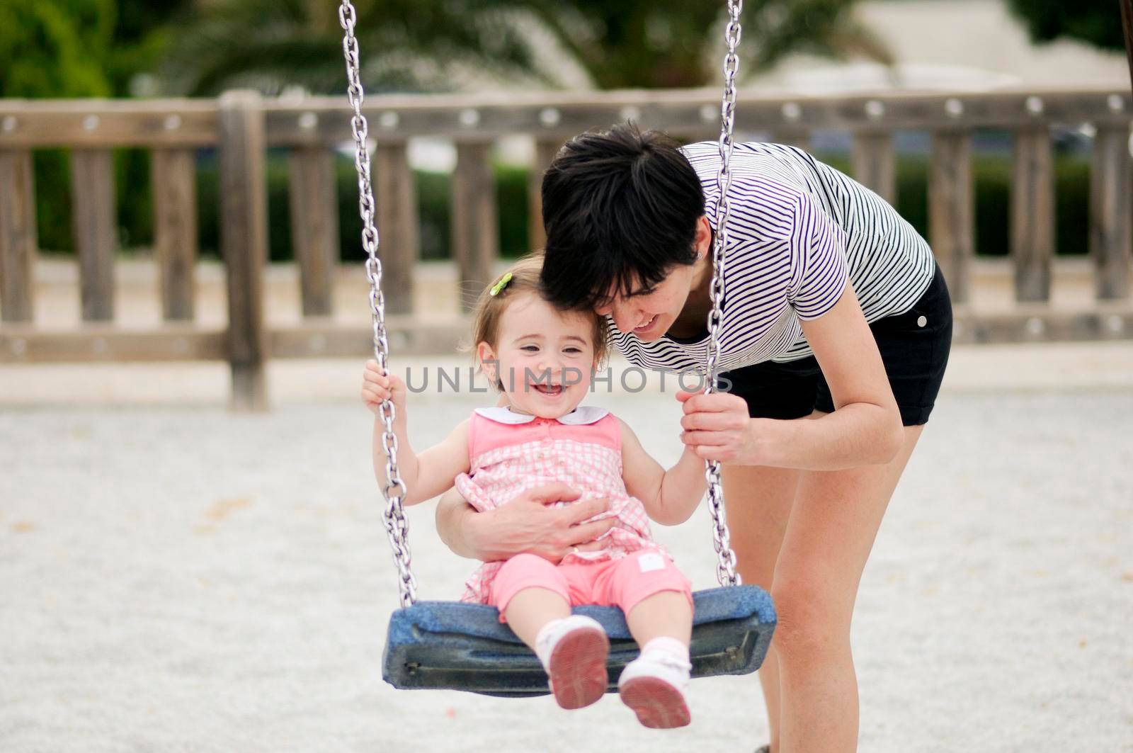 Mother swinging her little daughter on a swing in a playground