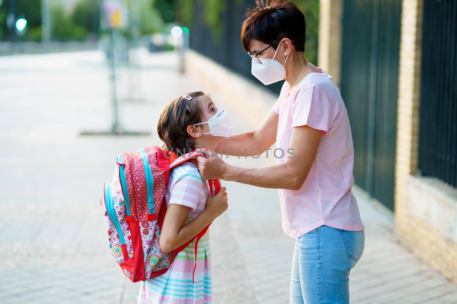 Mother preparing her little girl for the return to school wearing a mask. by javiindy