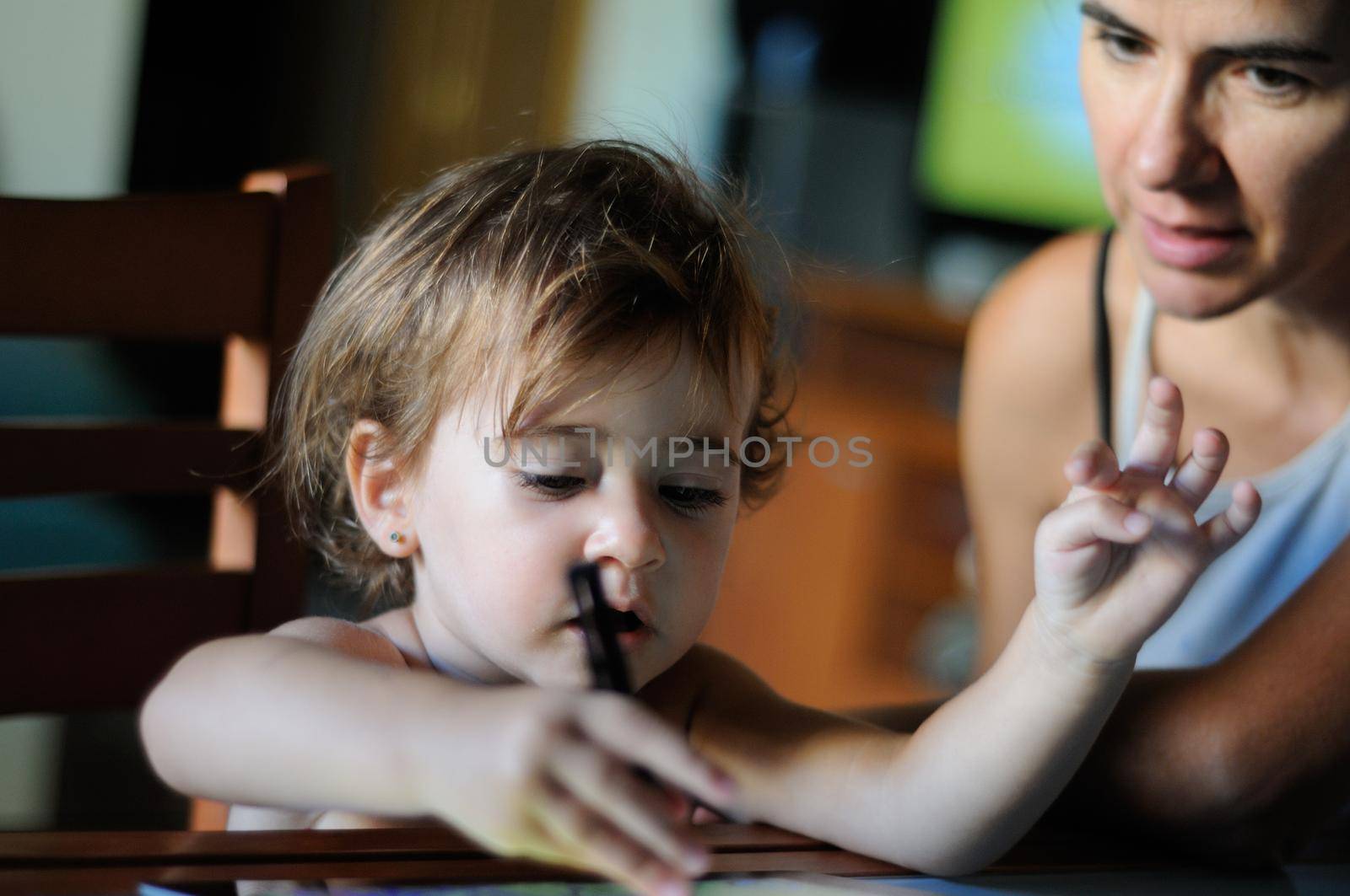 Little girl, two years old, painting with a digital tablet at home with her mother.